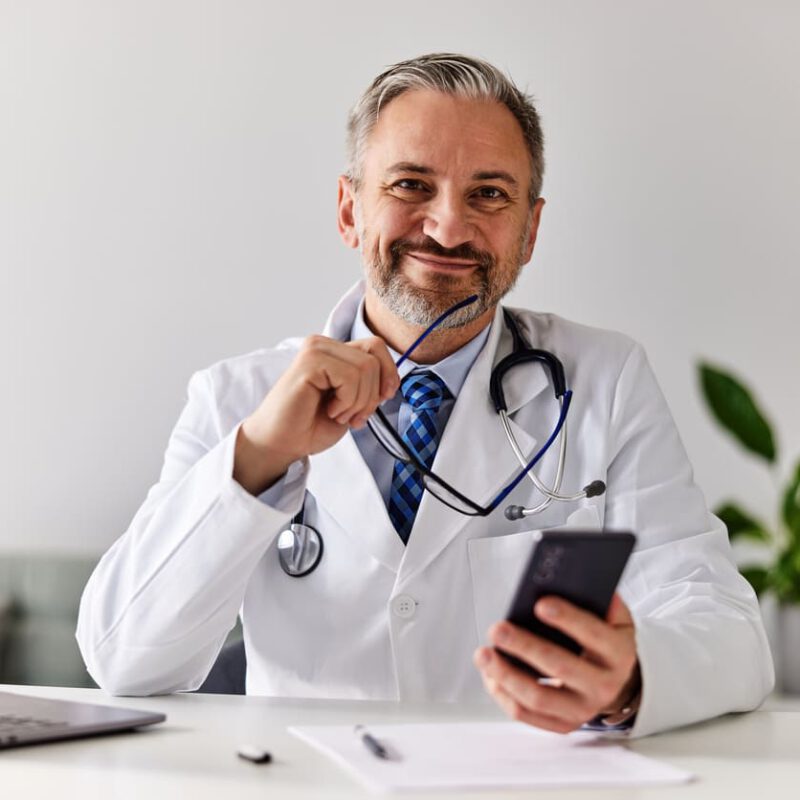 Symbolbild Klinikmarketing: Ein lächelnder Arzt schaut von seinem Handy auf